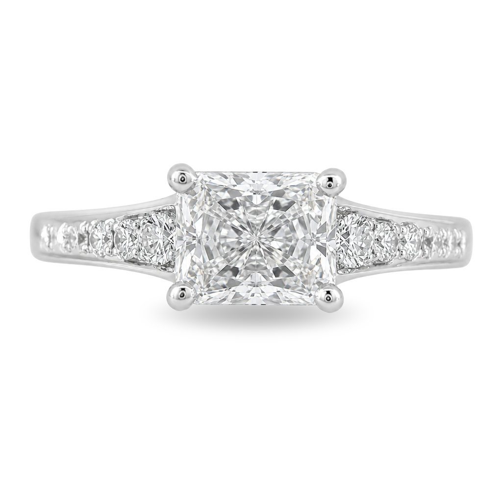 A radiant cut diamond engagement ring in a white gold band with pavé diamonds on either side, shown on a clean white background.