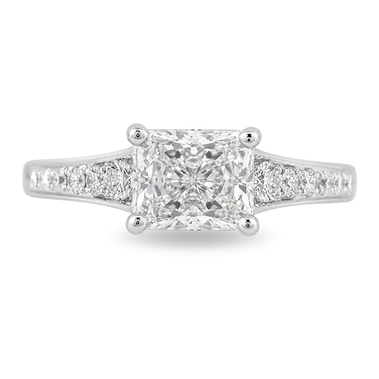 A radiant cut diamond engagement ring in a white gold band with pavé diamonds on either side, shown on a clean white background.